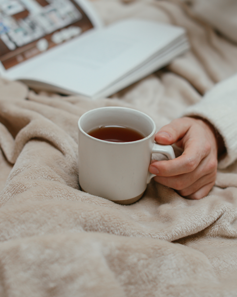 Photo d’une personne confortablement installée dans son lit avec une tasse de thé.